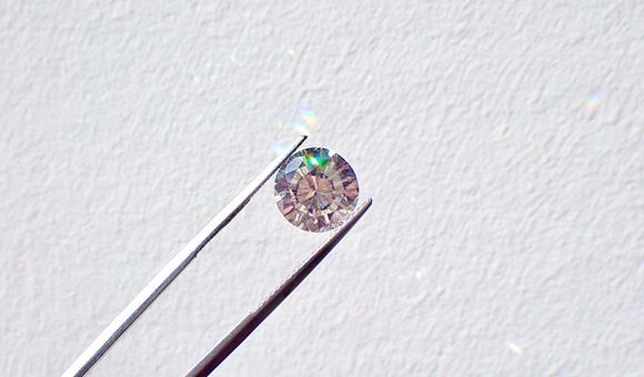Silver tweezers hold a small diamond against a white background.