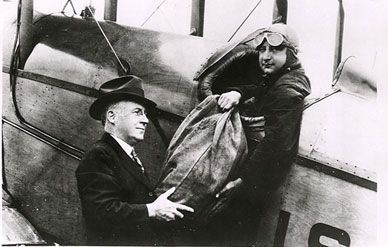 Reno, Nevada, Postmaster Austin Jackson (left) hands a mail bag to pilot Harry Huking in his DH-4 mailplane, July 1924.