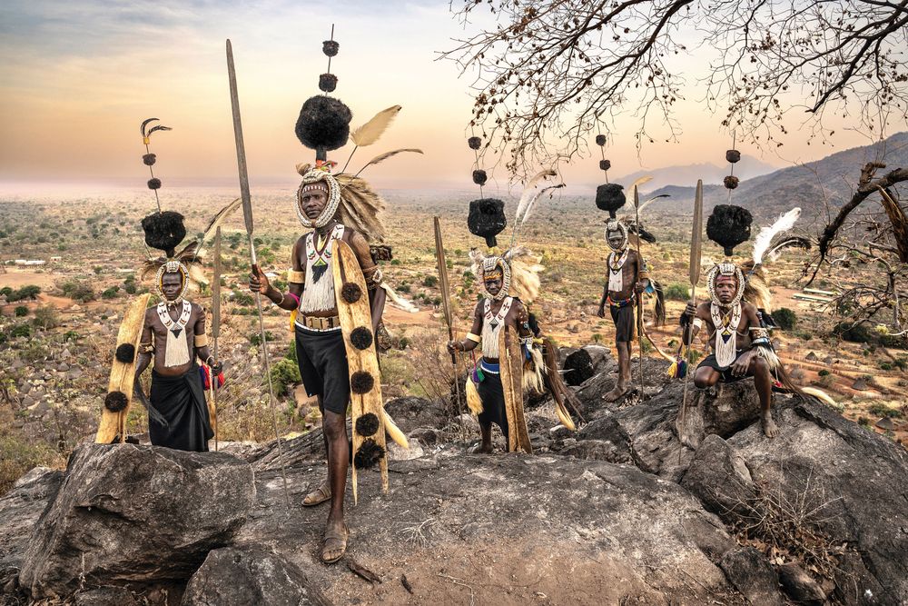 Lopit tribesmen at sunset (South Sudan). The Lopit are an ethnic group from Eastern Equatoria in South Sudan. They are traditionally agro-pastoralists who engage in farming and cattle herding.
Their homeland consists of hilly and mountainous terrain, which influences their way of life.
Despite modern influences, they continue to preserve their traditional beliefs, customs and social structures.

The Lopit have a rich cultural heritage with distinct traditions in music and dance. Drumming and communal dances play an essential role in their social gatherings. But mostly, the Lopit are known for the distinctive headdresses which are integral to their cultural attire. These headdresses are adorned with ostrich feathers are worn during significant ceremonies and dances, reflecting the community's values and social structures. They not only serve as decorative elements but also embody the wearer's status and role within the society, reinforcing cultural identity and continuity.