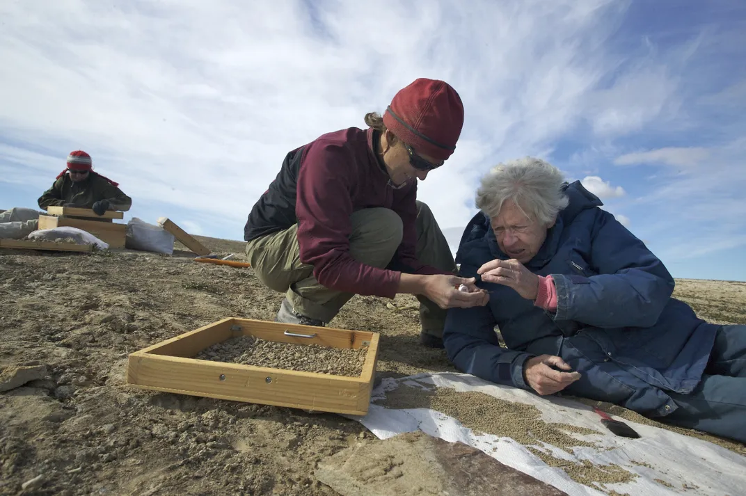 Two people on the ground looking at fossils