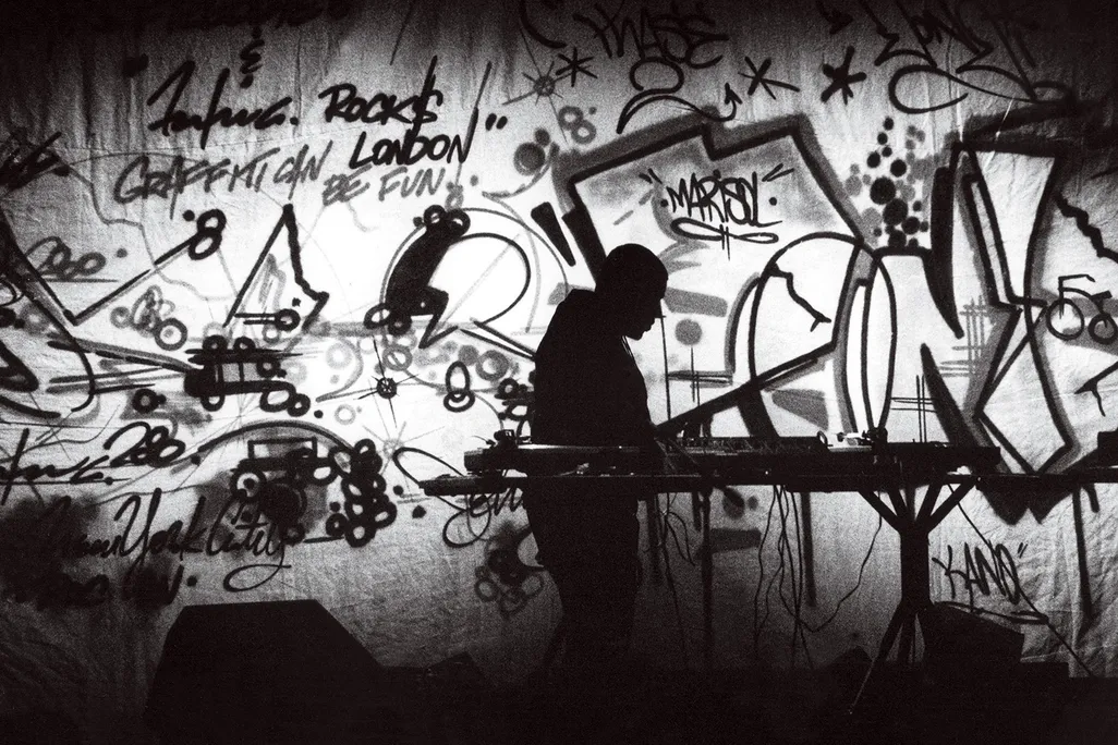 a black and white photograph of a DJ on stage surrounded by graffiti art