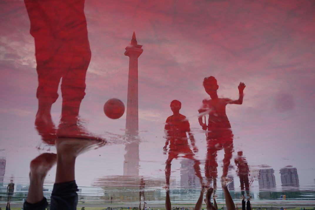 the reflection of young soccer players is captured in a puddle of rainwater