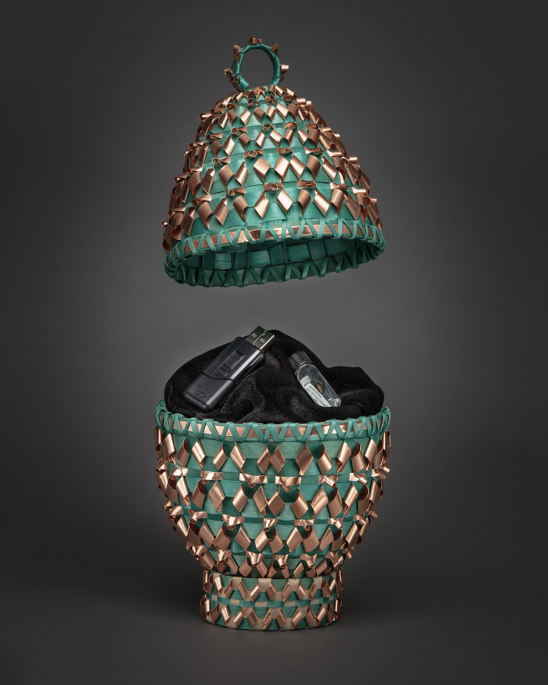Greed basket in the shape of an egg with coper and silver embellishments open to reveal a flash drive inside.