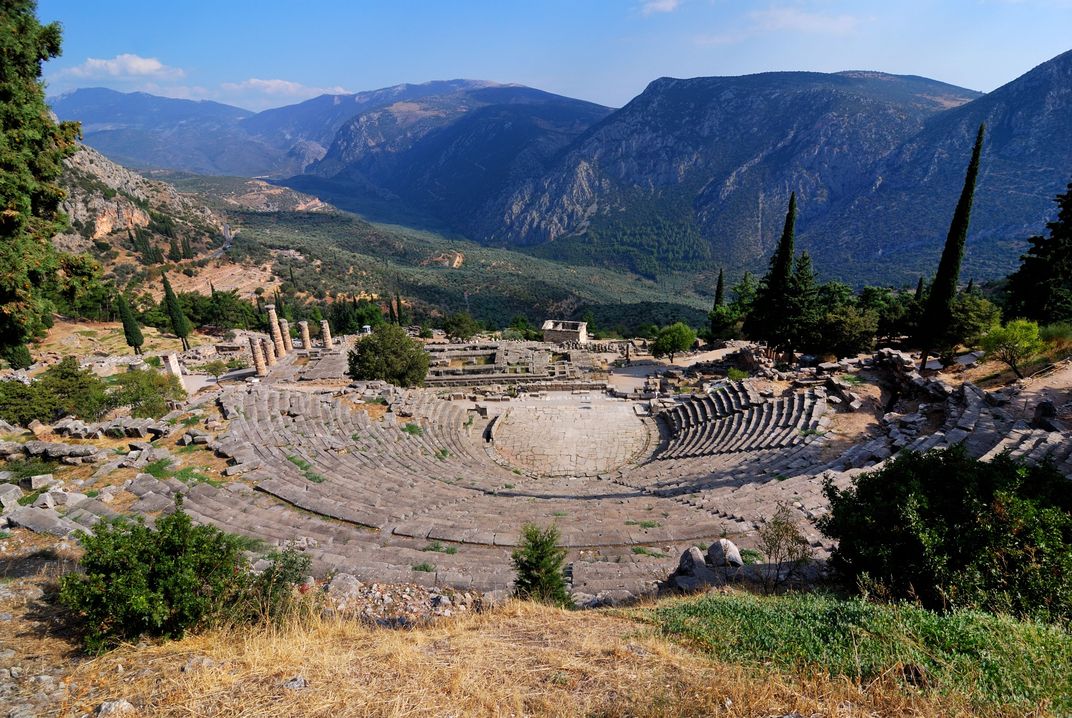 The stone theater built into the hillside with the Temple of Apollo and mountains in the background