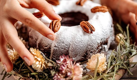 A hand places a pecan on a decadent dessert