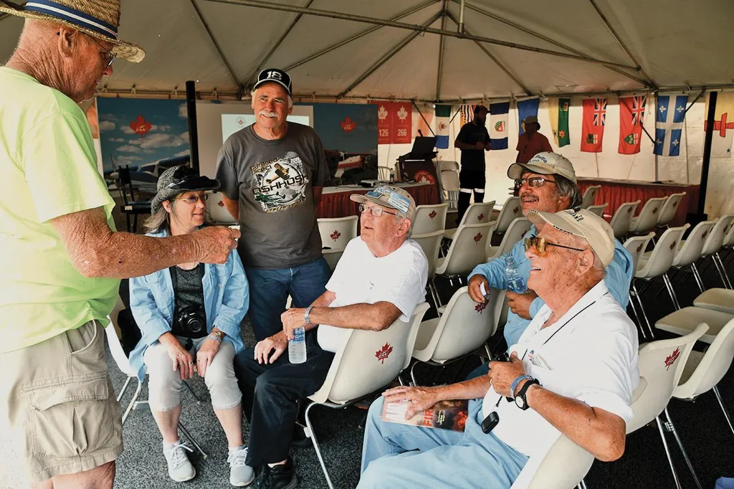 crowd of middle-aged to elderly people sitting and standing and talking at Oshkosh