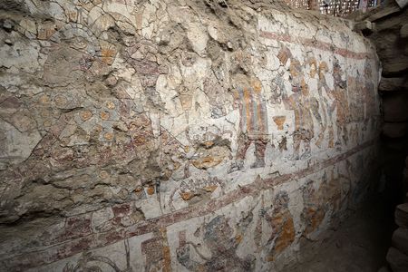 A painting of a crowned woman with scepter (upper left), a procession of men behind her carrying objects (upper right) and a textile workshop (below) on the wall of an ancient throne room in Peru