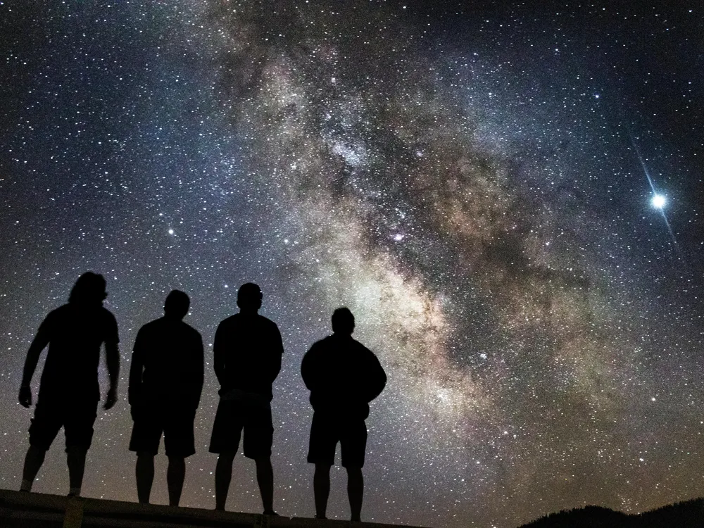 silhouettes of four people stand looking at the milky way