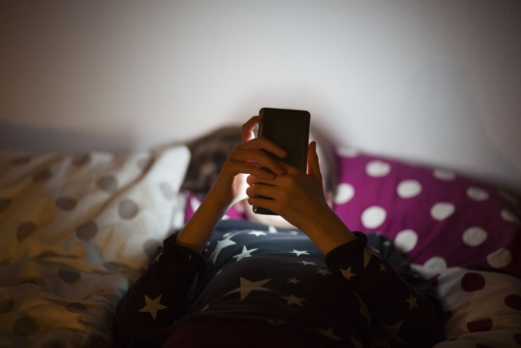 A young girl lying in bed with a phone in front of her face