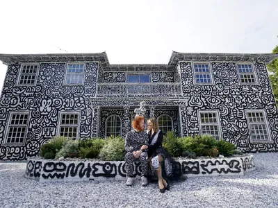 English artist Sam Cox and his wife, Alena, sitting in front of their Kent mansion, which Cox covered in doodles