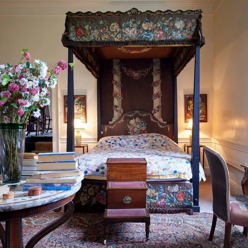 An ornate four-cornered bed with a colored quilt and surrounded by embroidered hangings with flower motifs