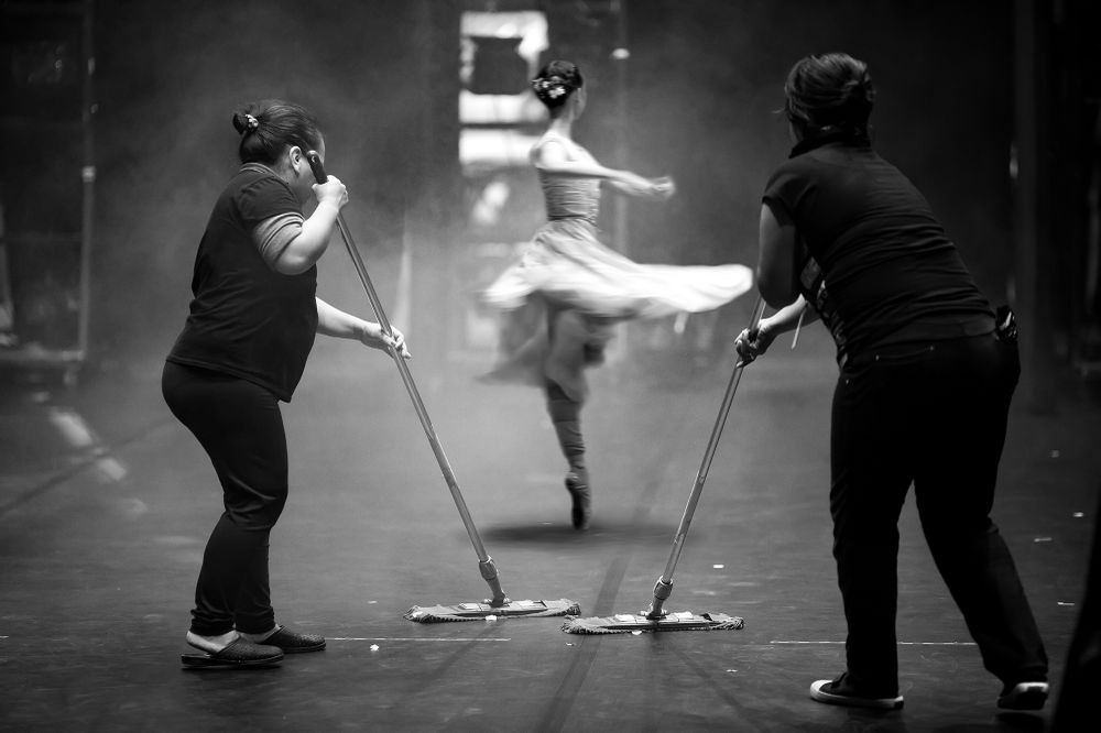 The photograph shows a ballerina rehearsing before a performance. Cleaning the stage and the ballet turned out to be curling.