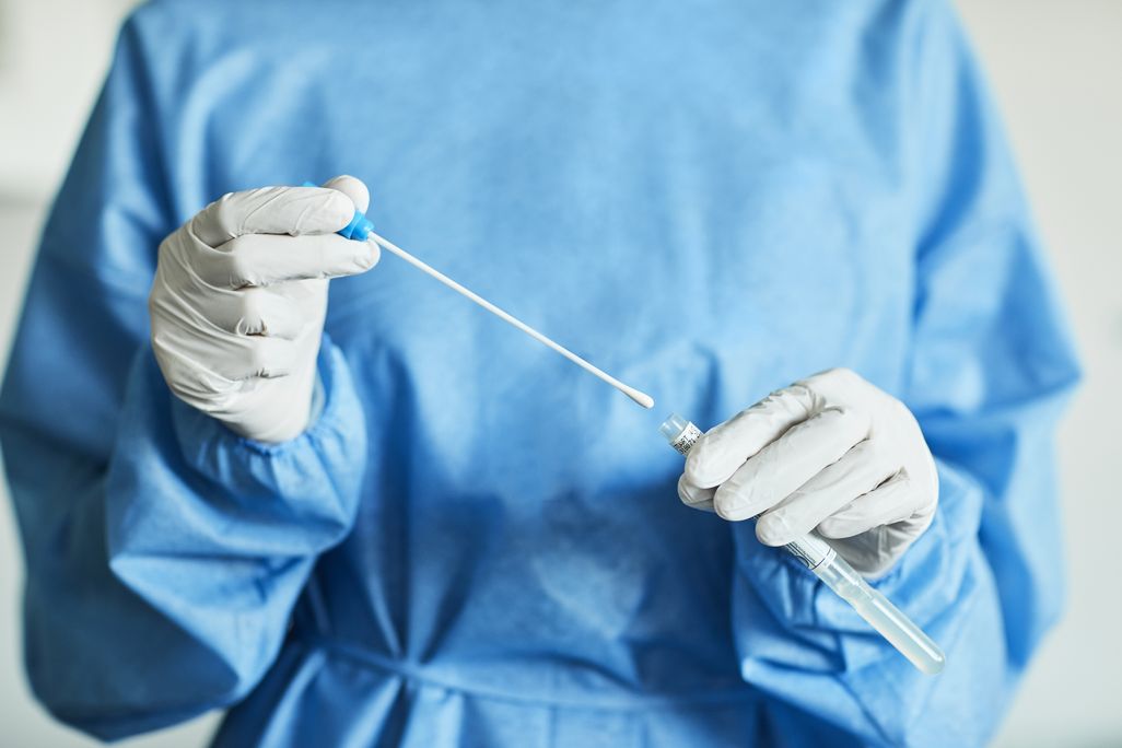 A female doctor in a blue surgical gown holding a long cotton swab used for covid-19 testing