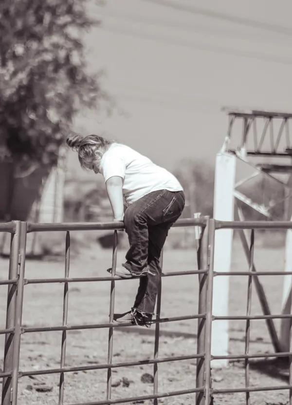 Young girl climbing a fence at a junior rodeo competition in Oklahoma thumbnail