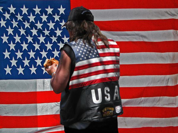 Veteran eating a hot dog, placed in front of an 'American flag. thumbnail