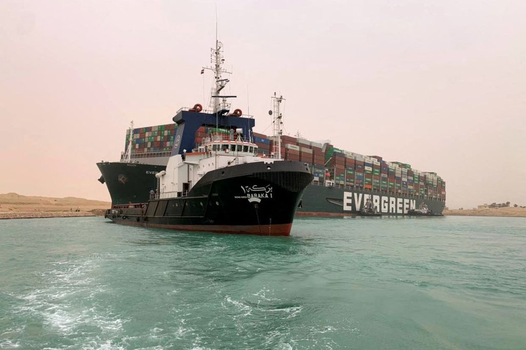 Pictures, is the shipping vessel, the Ever Given stuck on the Suez Canal. There is a tugboat pictured in front trying to pull it free