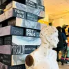 A pop-up museum display, featuring a tower of several “bricks” stacked like Jenga pieces. Each brick has writing on it: Fomo, body image, masculine marketing, pick-me girls, female sexuality, gender roles, a mother’s influence.
