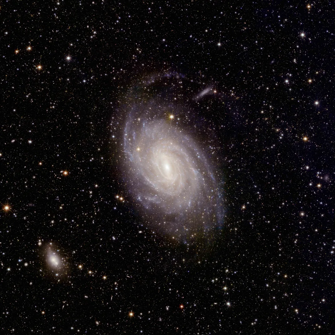 a spiral galaxy appears blue-white with its core shining brightly against a backdrop of other galaxies and darkness