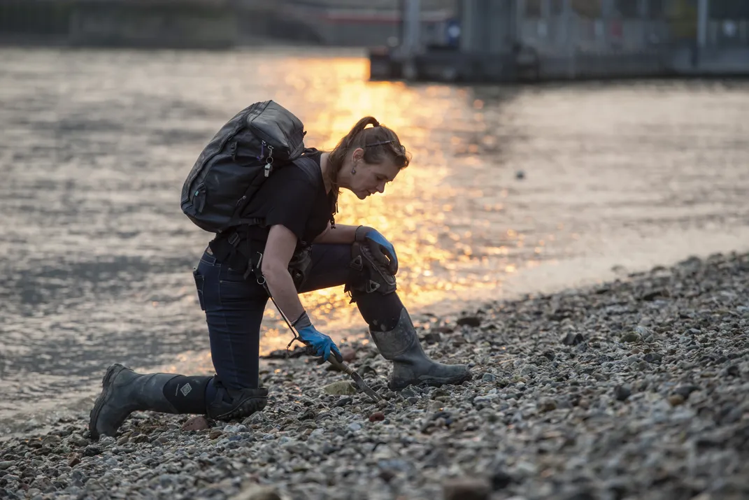 Mudlark Monika Buttling-Smith kneels on a rocky shore, collecting objects.