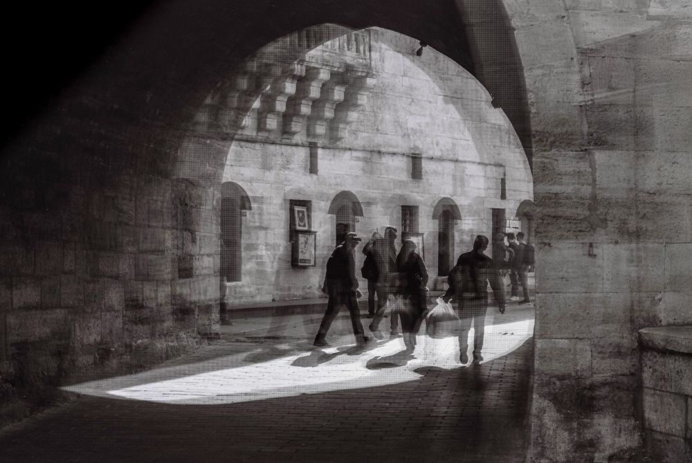 Created using analog double exposure, this image layers multiple passersby beneath a stone archway, compressing separate moments into one frame. The merging of figures and architecture reflects the continuity of human presence within historic spaces, where individual lives pass quickly but collective memory endures.