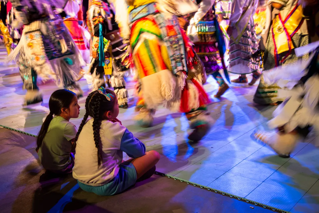 9 - Two young girls sit along the edge of a dance floor watching the ceremonial procession that marks the beginning of a powwow in Albuquerque.