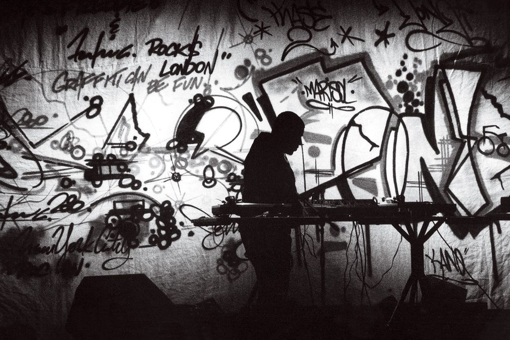 a black and white photograph of a DJ on stage surrounded by graffiti art