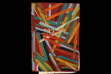 A photograph of a red book that reads, “Daily Reminders 1982” in white lettering. The book has yellow, green, blue, red, and orange strips of paint on it.