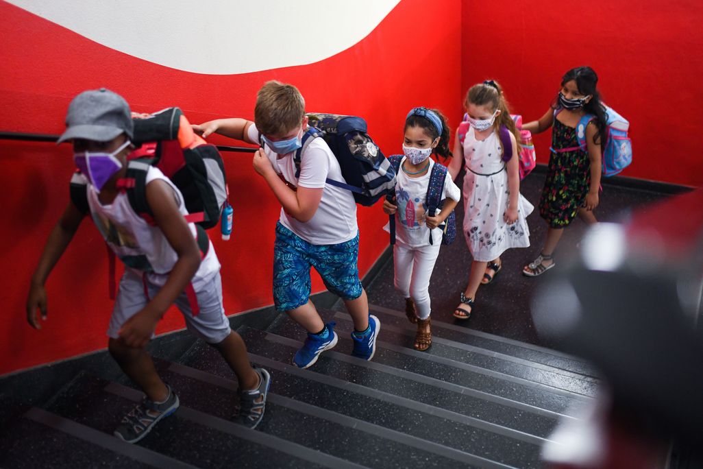 A row of children wearing masks walk up a staircase in a school.