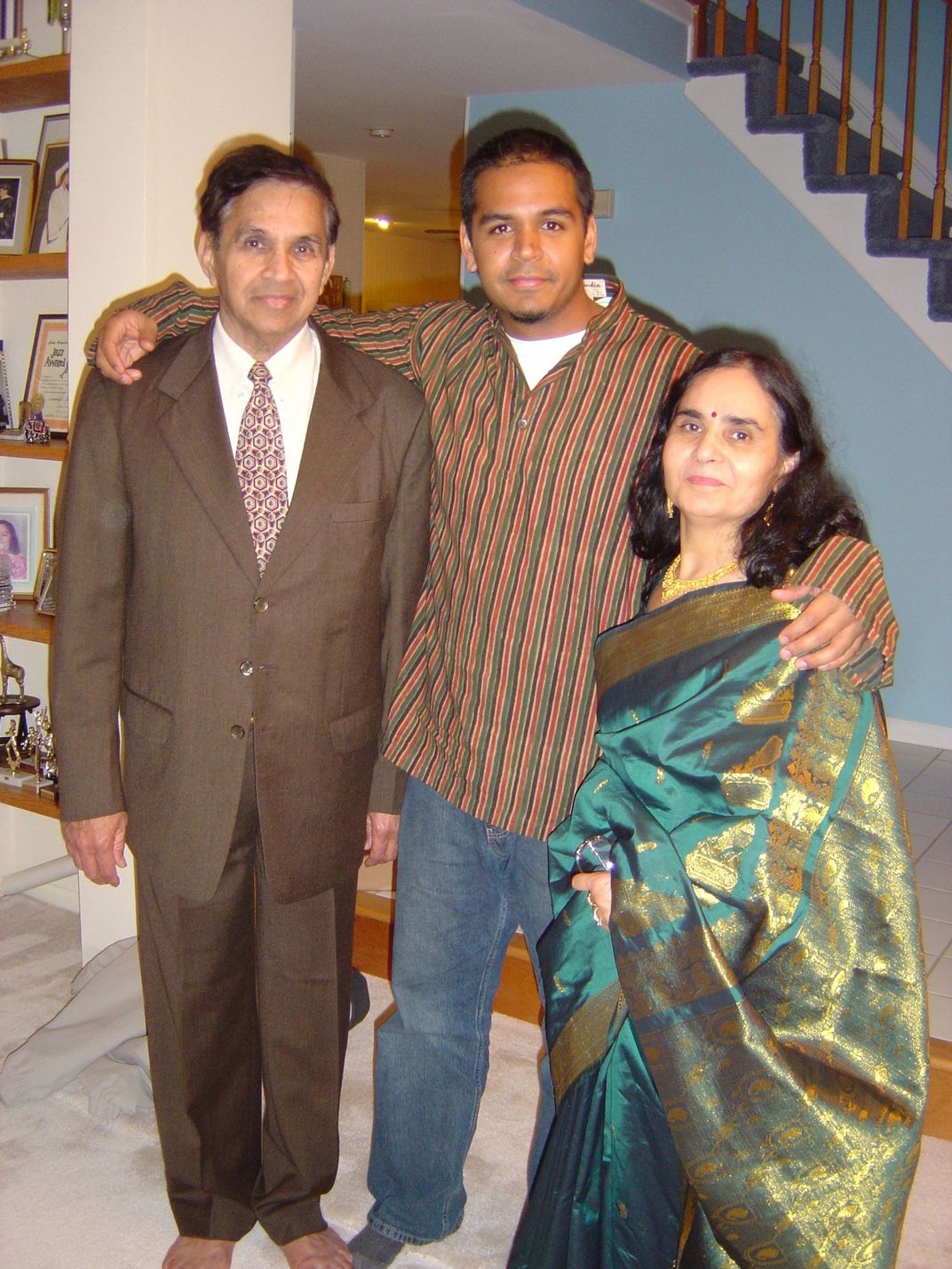 Photo of the author posing with his arms around his mother and father. They are all dressed up for a special occasion, the men in Western dress suits and the mom is traditional South Asian dress.