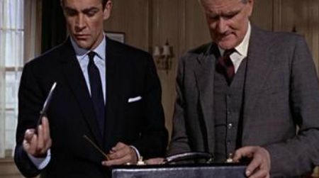 Desmond Llewelyn as Q in License to Kill showing Bond (Timothy Dalton) the camera gun that, when put together, became a sniper rifle.
