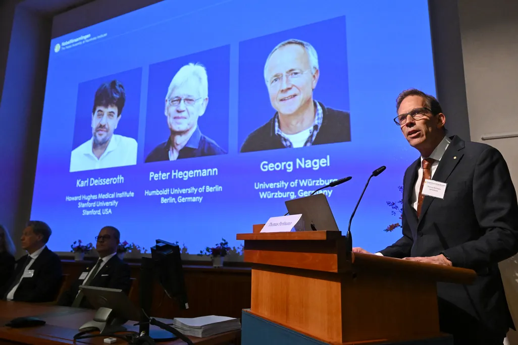 person standing at a podium with a projection of the three winners' headshots and names behind him