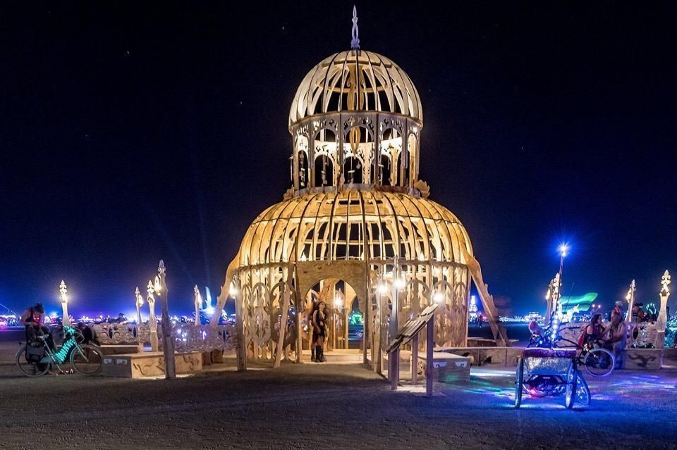 A photograph of a wooden temple being built at night in the dessert. 