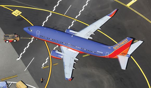 A twin-engine jet airliner painted in a livery of purple, red, and orange is parked on an airport ramp. The tail of the airline is marked with the word “Southwest.”
