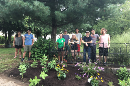 A group of young people stand in front of a pollinator garden in Lowell, MA