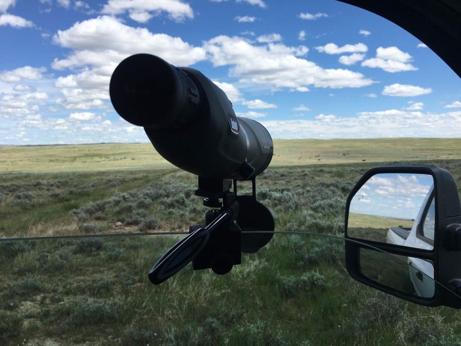 A spotting scope attached to a partially rolled down car window looks out over American Prairie Reserve grasslands in Montana.
