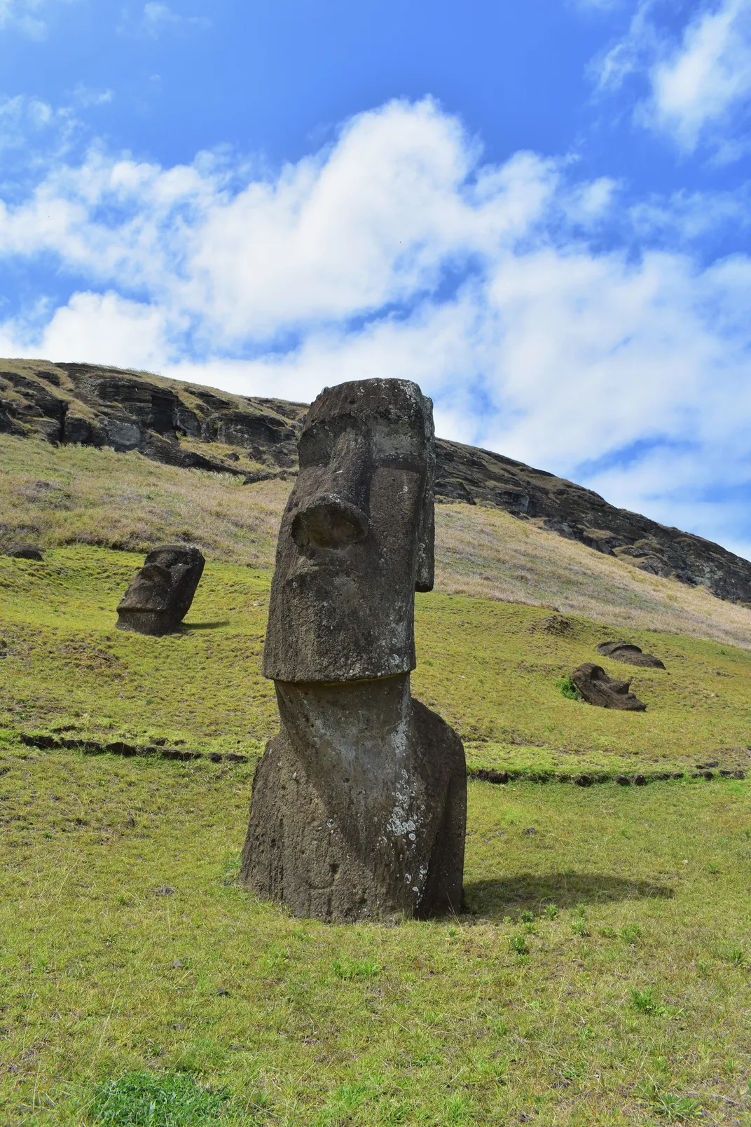 large stone heads and shoulders on a green hill with a partly cloudy sky