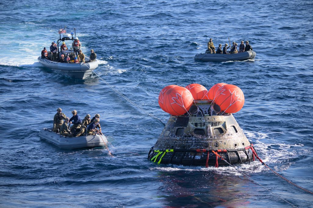 Three boats tug the Orion spacecraft in the ocean