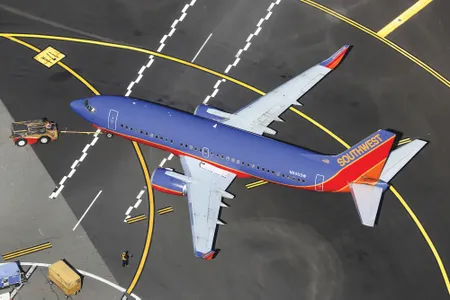 A twin-engine jet airliner painted in a livery of purple, red, and orange is parked on an airport ramp. The tail of the airline is marked with the word “Southwest.”
