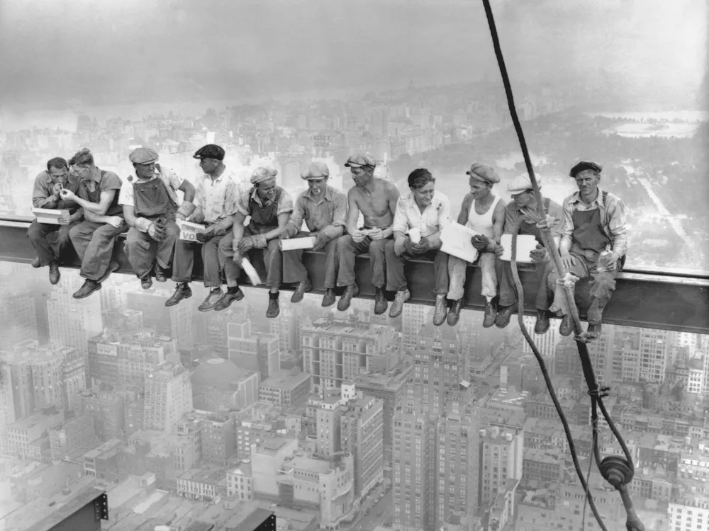 11 men sitting on a beam eating lunch above New York City
