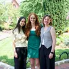 Three young women pose together for a photo in front of the Smithsonian Castle.