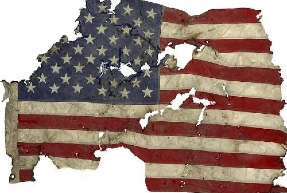 A tattered, torn, and singed American flag displayed against a white background.