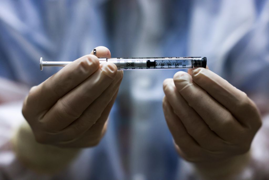 A pharmacy technician's gloved hands hold a dose of the Johnson & Johnson Covid-19 vaccine