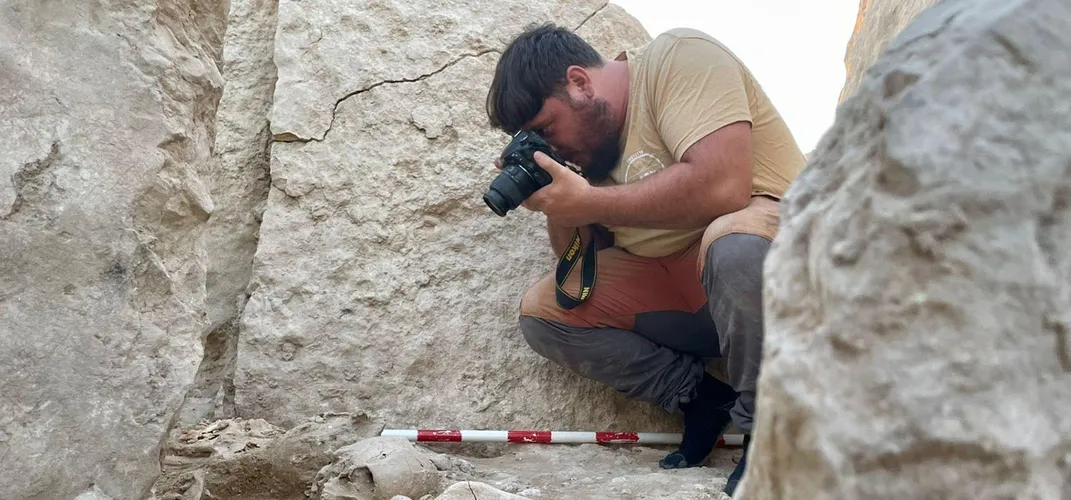 A person kneels among stones and photographs something on the ground