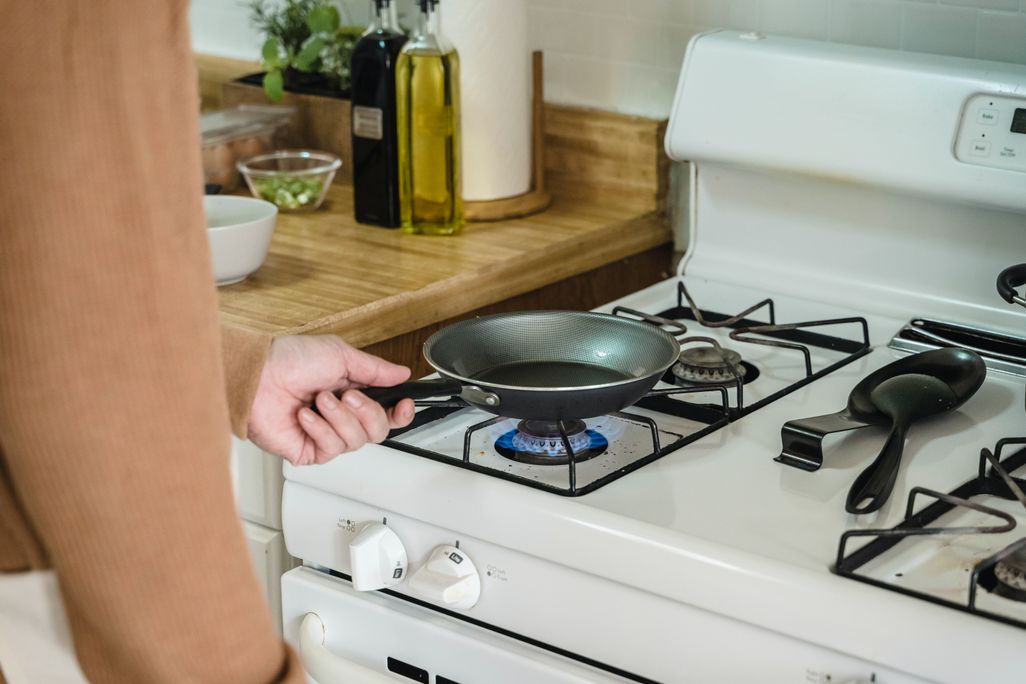 Person putting a frying pan on a white gas stove