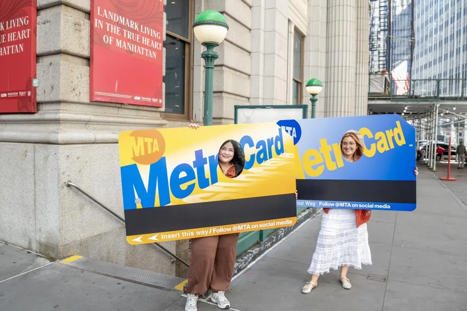 Two women posing with their heads in giant MetroCards