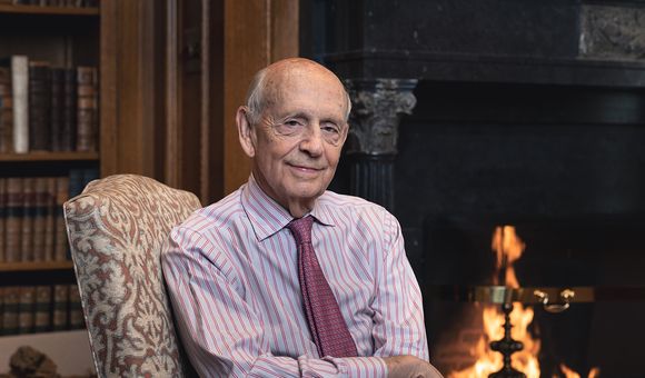 The cover of the book, Reading the Constitution, features Justice Stephen Breyer sitting in front of a blazing fire.