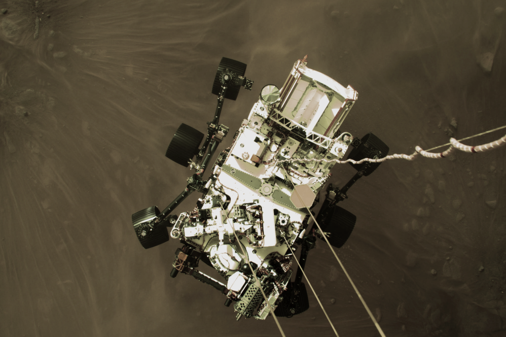 A photo taken during Perseverance's landing shows it dangling from cords above the surface of Mars