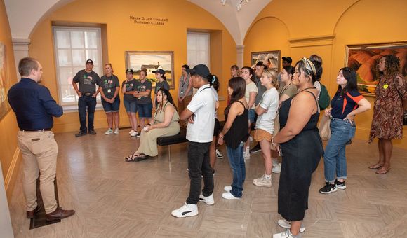 A man in a navy blue shirt and khakis leads a large group of students through an art gallery