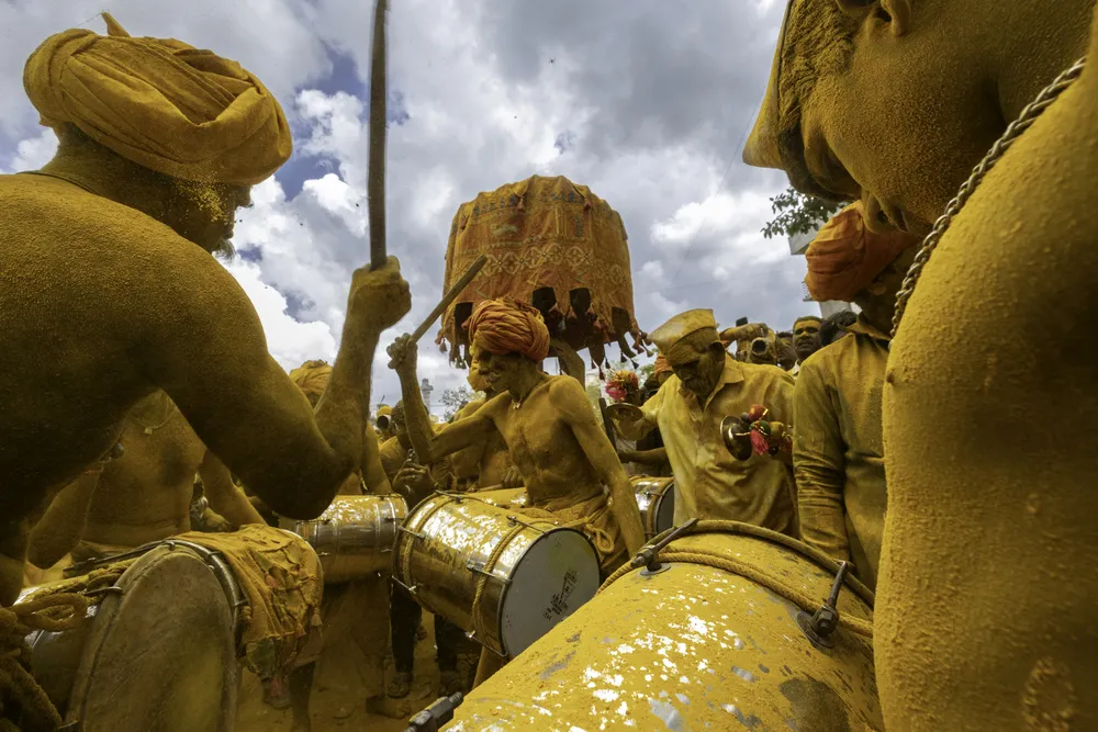 This vibrant photograph captures the fervor and cultural essence of the Shri Vittal Birdev Yatra at Pattankodoli, Maharashtra. Devotees, adorned in yellow turmeric powder, passionately beat drums in unison, filling the air with rhythm and reverence. The bright yellow symbolizes purity and devotion, as the community comes together to honor their deity in this dynamic celebration. The backdrop of traditional attire, energetic drumming, and swirling turmeric creates a mesmerizing scene of faith and festivity.