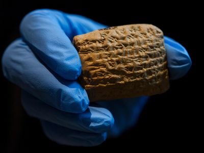 A museum worker wearing gloves holds up a cuneiform clay tablet, one of a collection of over 100, on display at a museum in Jerusalem.